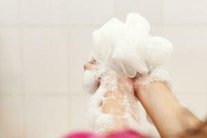 mulher lavando mãos com uma esponja dentro a banheiro. fêmea lavando braços com uma espumoso esponja dentro a banho. corpo Cuidado e limpar \ limpo conceito foto