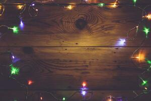 Natal decorativo luzes. Natal festão luzes em madeira. colorida natal luz lâmpadas em rústico Castanho prancha foto