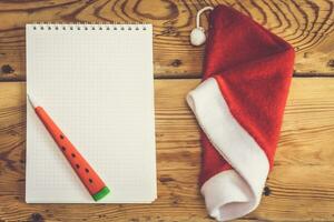 Natal e Novo ano fundo. em branco bloco de anotações, caneta e santa chapéu. Natal desejo lista. carta para santa claus foto