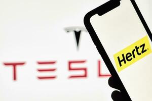 uma pessoa detém Smartphone com hertz marca comercial sobre grande Tesla logotipo foto