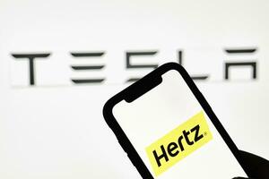 uma pessoa detém Smartphone com hertz marca comercial sobre grande Tesla logotipo foto