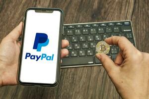 mão detém uma Smartphone com paypal logotipo e bitcoin foto