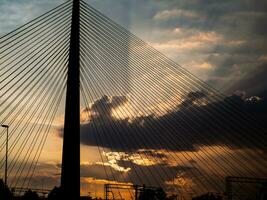 grande suspensão ponte torre às pôr do sol - raios solares estourando através a nuvens foto