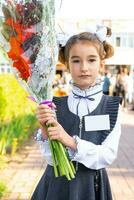 retrato do uma menina aluna do a 1º grau escola com branco arcos e flores dentro uma vestir unifor com crachá zombar acima. costas para escola, setembro 1, primeiro - nota. primário Educação, elementar aula. foto