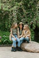 à moda caucasiano mãe e dela dois filhas estão conversando e caminhando dentro uma Primavera florescendo parque. mãe dia e uma feliz família foto