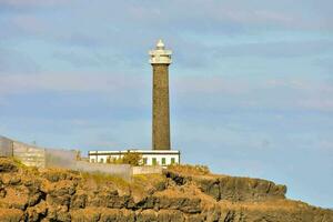 uma farol em topo do uma penhasco com uma pequeno construção foto