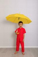 Garoto moda vestindo uma estilo chinês camisa segurando uma amarelo guarda-chuva poses para uma foto atirar.