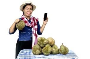 ásia mulher Vendedor de frutas aguarde durian fruta e Smartphone, ficar de pé ao lado frutas mesa, isolado em branco fundo. conceito, fruta vendedor usar Internet tecnologia dispositivo para vender agricultura cultivo conectados foto