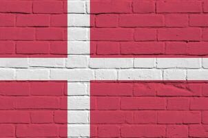 Dinamarca bandeira retratado dentro pintura cores em velho tijolo muro. texturizado bandeira em grande tijolo parede alvenaria fundo foto