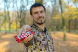 Carcóvia, Ucrânia - Outubro 21, 2019 jovem homem passes uma kit Kat chocolate Barra dentro a outono parque. a manifestação do gentileza, tratando com doces foto