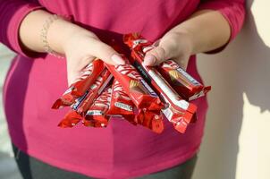 Carcóvia, Ucrânia - Outubro 21, 2019 uma jovem caucasiano morena menina detém muitos kit Kat chocolate bares dentro vermelho invólucro dentro luz sala. kit Kat chocolate fabricado de aninhar foto