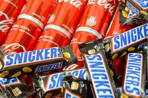 risadinhas chocolate bares dentro Castanho invólucro mentiras em vermelho coca Cola lata latas fechar acima. famoso beber e chocolate produtos foto