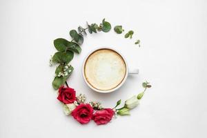 xícara de café branco com círculo de flores frescas em fundo branco foto