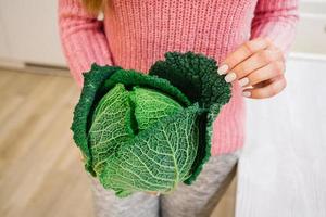 mãos femininas segurando uma cabeça de repolho verde foto