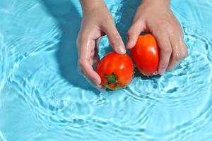 mulher lavando tomate na água. lave os vegetais antes de cozinhar foto