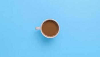 mão segurando uma caneca de café em um fundo azul foto