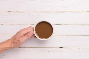 mão segurando uma caneca de café em um fundo de madeira foto