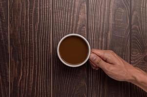 mão segurando uma caneca de café em um fundo de madeira foto