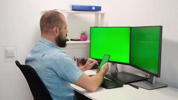 homem de negócios trabalhando e digitando no celular e no computador com dois monitores multitarefa tela verde foto