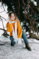 adolescente Loiras dentro uma amarelo suéter lado de fora dentro inverno. uma Adolescência menina em uma andar dentro inverno roupas dentro uma Nevado floresta foto