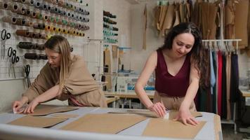 duas costureiras trabalhando com um pano e giz sobre uma mesa. costureira usa giz no contorno do padrão em tecido, no ateliê. alfaiate profissional, designer de moda no estúdio de costura.