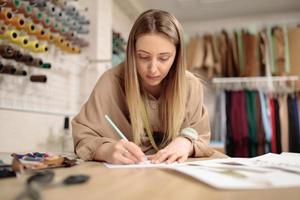 designer de moda jovem artista feminina está desenhando um esboço na mesa no estúdio moderno. pequeno alfaiate
