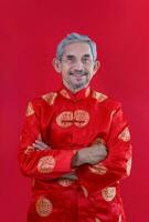 retrato ásia Senior homem com cinzento cabelo e barba dentro tradicional chinês roupas isolado em vermelho fundo foto