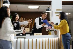 hotel convidado recebe cadastro Formato a partir de ásia masculino recepcionista para faço quarto reserva. sorridente fêmea porteiro dando direção para cliente às frente escrivaninha do acolhedor recorrer foto