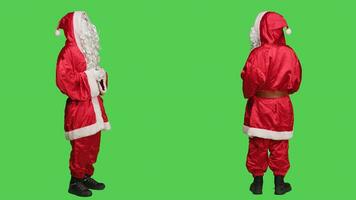 santo usuario personagem rindo em Câmera, dizendo ho ho ho e espalhando Natal espírito durante inverno feriados. jovem homem vestido Como santa com vermelho traje e chapéu, cheio corpo tela verde. foto