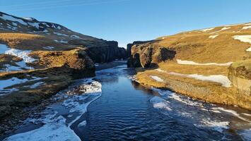 islandês desfiladeiro com congeladas água corrente fluindo baixa entre montanhas coberto dentro neve, criando mágico contexto. mágico fjadrargljufur desfiladeiro com rio dentro Islândia, passeio turístico. foto
