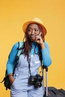 africano americano mulher viajando fora do país, posando dentro estúdio com dslr Câmera e carrinho bolsas. fêmea viajante indo em internacional cai fora para final de semana Atividades, urbano destino. foto