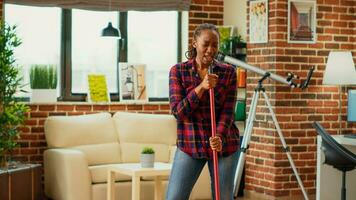 africano americano dona de casa ouvindo para música e esfregar apartamento pisos, usando esfregão e lavando solução. jovem feliz mulher dançando e cantoria, tendo Diversão com Primavera limpeza. foto