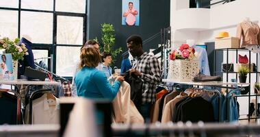 ásia à moda empregado ajudando casal com formal roupa, discutindo mercadoria tecido dentro moderno boutique. africano americano clientes compras para elegante roupas dentro roupas loja foto
