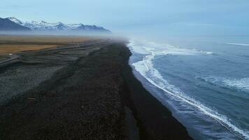 islandês Preto areia de praia zangão tomada, lindo litoral com ondas falhando em atlântico costa. nórdico panorama com Nevado montanhas e Preto areia em praias, cênico rota. lento movimento. foto