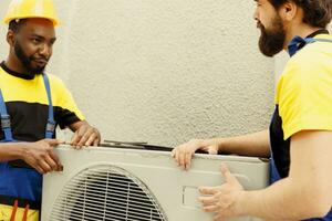 africano americano reparador e Aprendiz trabalhador puxar separado velho defeituoso ao ar livre hvac sistema para substituir isto com Novo desempenho condensador depois de drenando refrigerante e substituindo canalização foto