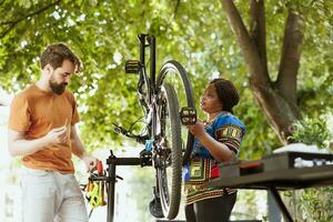 multirracial namorada e namorado usando profissional equipamento para consertar quebrado bicicleta pneu e roda dentro casa quintal. jovem casal utilizando vários Ferramentas para bicicleta manutenção ar livre. foto