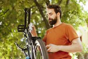 desportivo dedicada homem utilizando especializado lubrificante para graxa dele bicicleta corrente. a imagem monitores caucasiano homem habilmente lubrificação dele bicicleta cadeia anel para uma desatado ciclismo experiência. foto