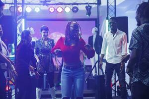 mulher clubber mostrando movimentos às improvisado dança batalha para diverso amigos dentro Boate. africano americano dançarino festa em pista de dança iluminado com etapa holofotes dentro clube foto