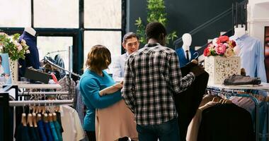 ásia Gerente ajudando clientes com roupas, explicando roupas tecido dentro compras loja. africano americano casal comprando elegante equipamento e à moda acessórios dentro moderno boutique. moda conceito foto