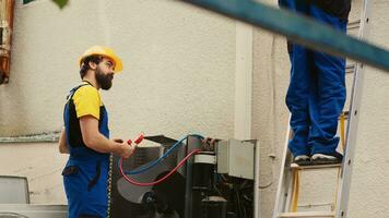 capaz eletricista medindo Freon níveis dentro condensador com múltiplo metros enquanto africano americano colega passos baixa a partir de dobrando escada depois de acabamento verificação telhado hvac sistema foto