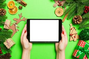 vista superior da mulher segurando o tablet nas mãos sobre fundo verde feito de decorações de natal. conceito de férias de ano novo. brincar foto