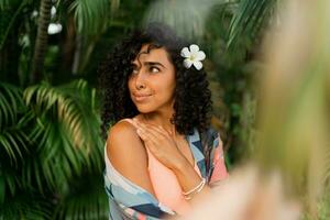 fechar acima retrato do feliz mulher com plumeria flor dentro cabelos depois de spa dentro luxo recorrer. vestindo boho tropical roupa. foto