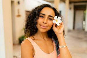 fechar acima retrato do lindo mulher com tropical flor dentro mão posando dentro luxo spa hotel. spa e corpo Cuidado conceito. foto