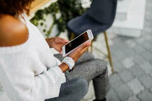 fechar acima do mulheres mãos segurando célula Telefone com em branco cópia de espaço scree para seu publicidade texto mensagem ou promocional contente, Preto menina assistindo vídeo em Móvel telefone durante café pausa. foto