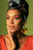 Preto africano americano mulher dentro laranja roupas e étnico cabeça embrulho Eu cutucando dentro estúdio. brilhante faço acima. foto