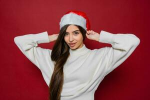 lindo europeu mulher com grandes cabelos dentro santa chapéu posando dentro estúdio em vermelho fundo. foto