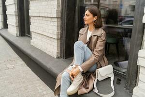 confiante curto cabelos mulher vestindo na moda bege cor casaco, branco texturizado couro ombro bolsa, caminhando dentro rua do europeu cidade. outono moda tendências. foto