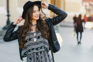 lindo surpreendente morena mulher com grandes ondulado Penteado dentro Primavera ou outono à moda urbano equipamento caminhando em a rua. vermelho lábios, fino corpo. rua moda conceito. foto