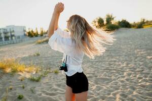 à moda bem torneado menina com retro Câmera posando em ensolarado tarde de praia. tropical humor. foto