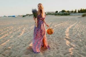 cheio comprimento imagem do Loiras mulher com ramalhete do lavanda caminhando em a de praia. pôr do sol cores. foto